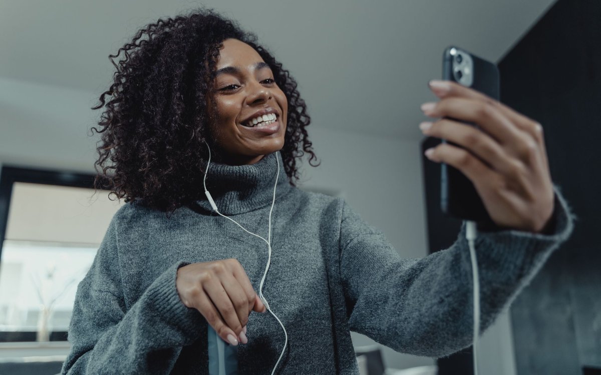 Mujer sonriendo durante una videollamada desde su celular con audífonos puestos