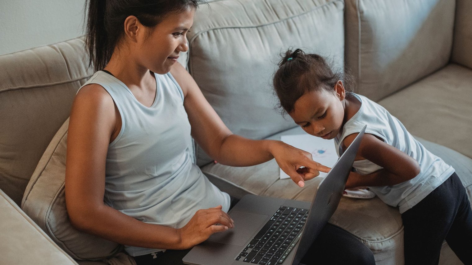 Madre e hija frente a una computadora en el sofá de su casa